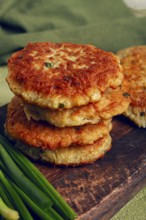Crispy potato pancakes Latkes, stacked on a wooden board next to fresh green onions, natural light,