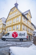 A DPD delivery van stands in front of a yellow-painted half-timbered building covered in snow,