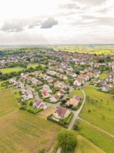 Residential area with densely built houses and streets, surrounded by fields under a slightly