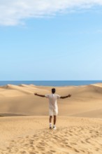 Young man opening arms in maspalomas dunes, gran canaria, feeling freedom and enjoying the desert