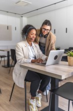 Two female customer service representatives collaborating on a laptop, providing assistance and