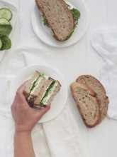 Hand picking from a platter of cucumber and spinach vegetarian sandwich