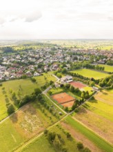 Aerial view of a town with neighbouring fields and a tennis court, surrounded by green vegetation