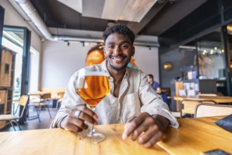 Happy customer is holding a glass of beer while sitting at a table in a modern and stylish