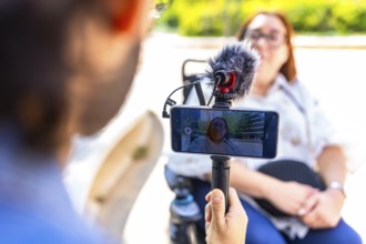 Videographer holding a smartphone on a tripod with external microphone, recording an interview with