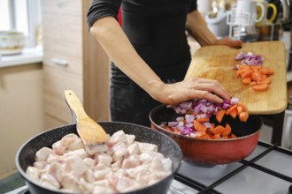 Unrecognizable woman cooking chicken pieces in one pan while pouring chopped onions and carrots to