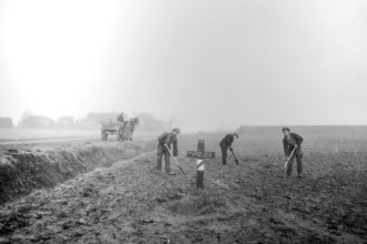 Wooden cross on grave of fallen soldier and workers levelling field on former battlefield after the