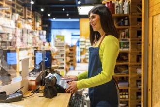 Smiling saleswoman using a digital checkout in an organic supermarket or grocery store, selling