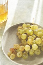 A branch of white grapes, on a gray plate, with a glass of white wine, top view, natural light,