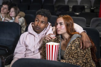 Young multi ethnic couple watching a movie in cinema, eating popcorn and enjoying their time