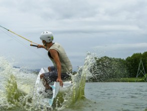 Young man jumping into the lake with a wakeboard, water sports, water skiing in the wake park