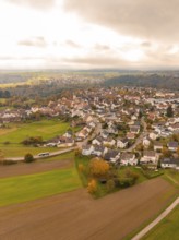 Aerial view of a village surrounded by autumnal fields under a cloudy sky, Tiefenbronn, Germany