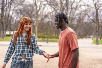 Young interracial couple holding hands and smiling while walking in a park, enjoying a romantic
