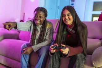 Two friends enjoying their free time playing video games at home, sitting on a comfortable sofa in