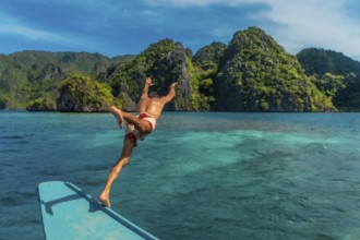Young man diving from traditional bangka boat into the turquoise waters of coron island,