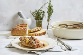 Cooked rabbit stew is served on a plate with herbs on top. Fresh bread is placed next to the dish
