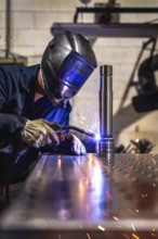 Vertical photo of a concentrated male caucasian welder with protective gear working in a factory