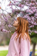 Young woman with long red hair, wearing pink hooded sweatshirt, breathing fresh air and enjoying