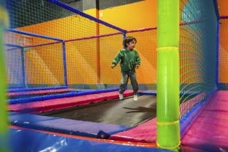 Young boy enjoying playtime, bouncing on a trampoline inside a vibrant and safe indoor play area