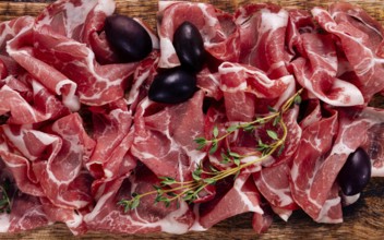 Freshly cut dried meat, served with olives and herbs, on a wooden chopping board, no people