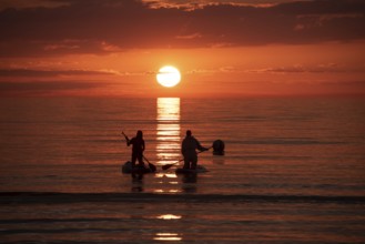 Two people paddling in the calm sea at sunset on stand-up paddle, silhouettes against a bright
