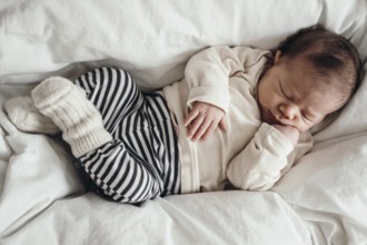 Sleeping baby in a striped romper lying on a white bed, looks peaceful and secure