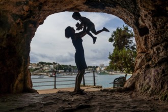 Silhouette of a mother lifting her son inside a cave with a view of the harbor in puerto cristo,