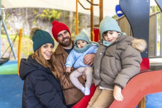Smiling family bundled in winter clothes, enjoying quality time together while playing on a