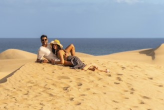 Couple relaxing on the warm sand of maspalomas dunes, enjoying the stunning ocean view and creating