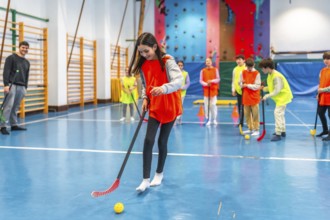 Elementary school students learning and playing floorball in a gym class with their teacher