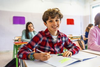 Happy elementary school student smiling and writing in notebook during class, with classmates in