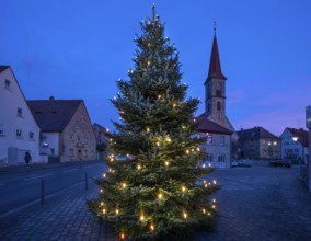 Illuminated Christmas tree on the village square at dusk, St Bartholomew's Church in the