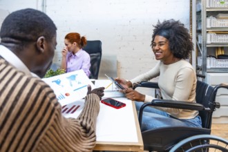 Cheerful and smiling african woman with disability sitting on wheelchair and colleague discussing