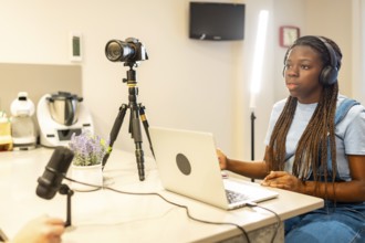 Young woman recording a vlog using a laptop, camera, microphone, and headphones in a home studio