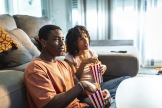 Young couple enjoying a movie night at home, sitting on the sofa, eating popcorn and watching