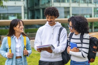 Happy multi-ethnic university students reading notes together standing outside the university in a