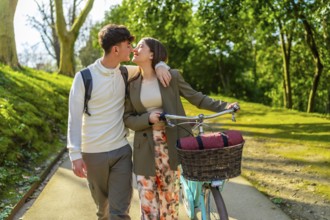 Romantic couple sharing a tender kiss while strolling through a park with their bicycle, enjoying a