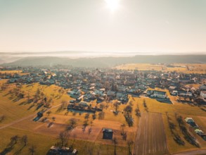 View of a village surrounded by fields and trees in the warm autumn light, Neubulach, Black Forest,