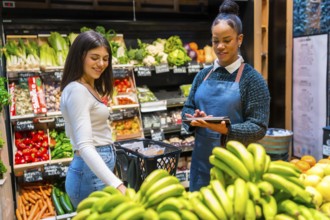 Supermarket employee using tablet helping customer buying bananas in grocery store with fresh