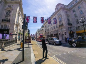 Businessman using smartphone on a london street decorated with british flags, with typical red bus