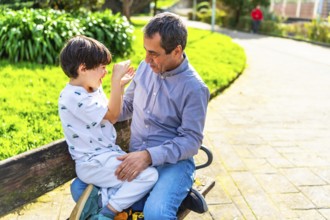 Grandfather and grandson enjoying a playful moment together, sitting on a park bench surrounded by