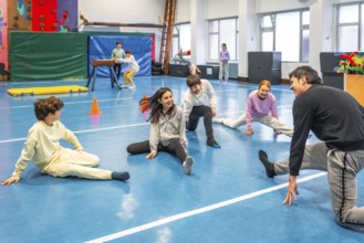 Group of smiling students practicing stretching exercises with their teacher during physical