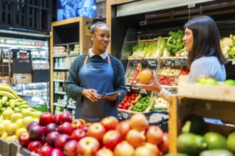 Supermarket employee assisting customer with grapefruit selection while checking prices and