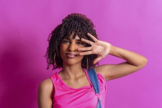Young woman with curly hair and pink top partially covering her face with her hand on a vibrant