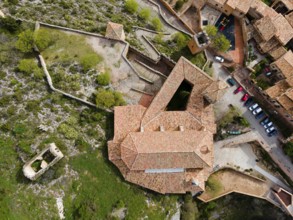 An aerial view of a historic fortress with tiled roofs and surrounding buildings on stony terrain,