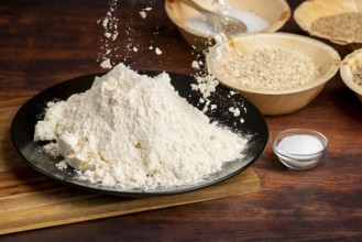 Flour is sprinkled over curd cheese, surrounded by baking ingredients on a wooden table