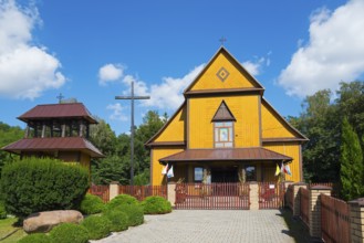 Yellow wooden church in summer under a blue sky with a wooden fence and surrounded by trees, Church