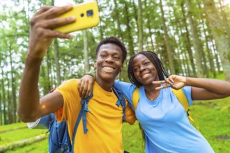 Cheerful african friends taking selfie gesturing victory with hand while hiking in the forest