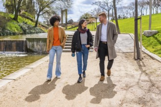 Three young professionals are enjoying a walk and conversation together in a sunny park, strolling