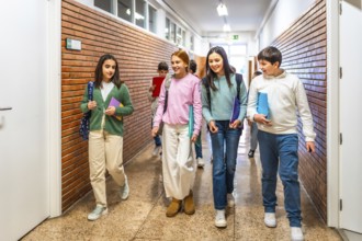 Group of cheerful students walking together in school hallway, carrying books and backpacks,
